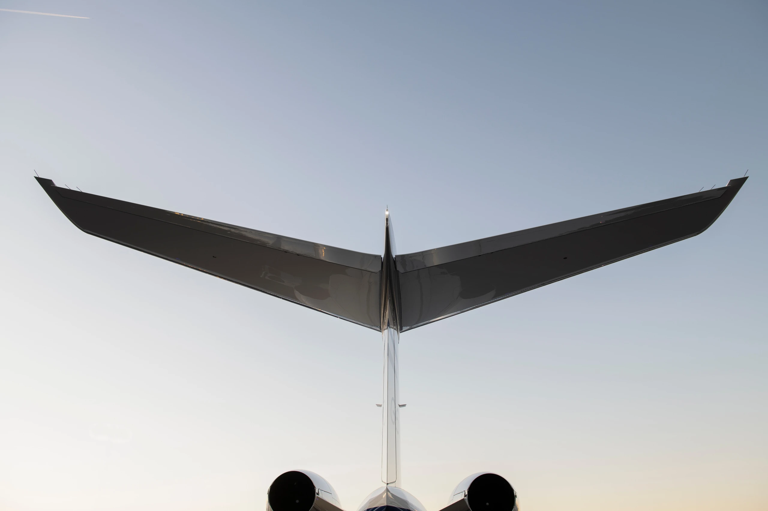 The image shows the tail of an airplane, prominently featuring the T-tail design against a clear sky. The airplane engines are partially visible below the tail.